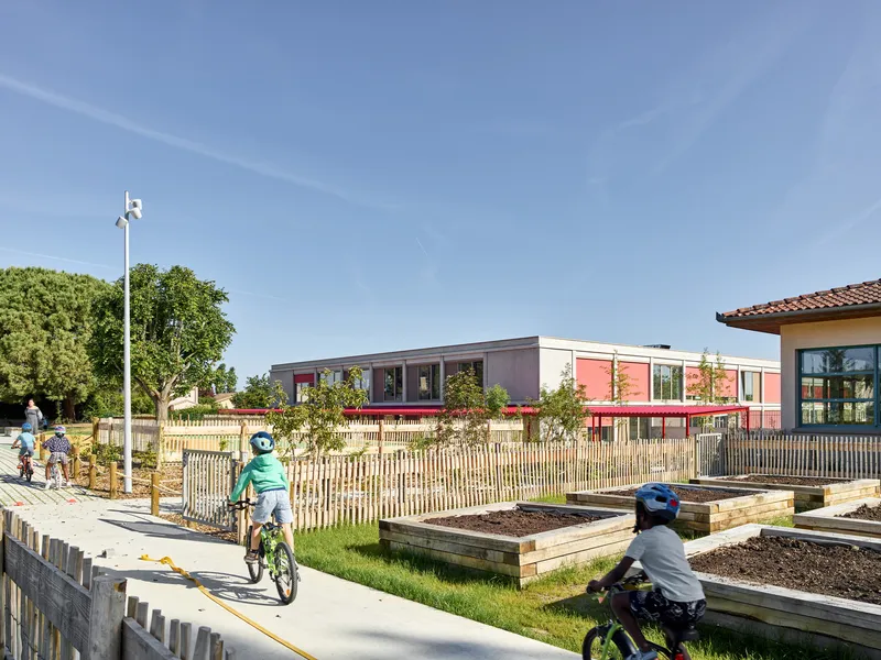 Distant view of the low-rise building with children cycling along the timber-fenced path