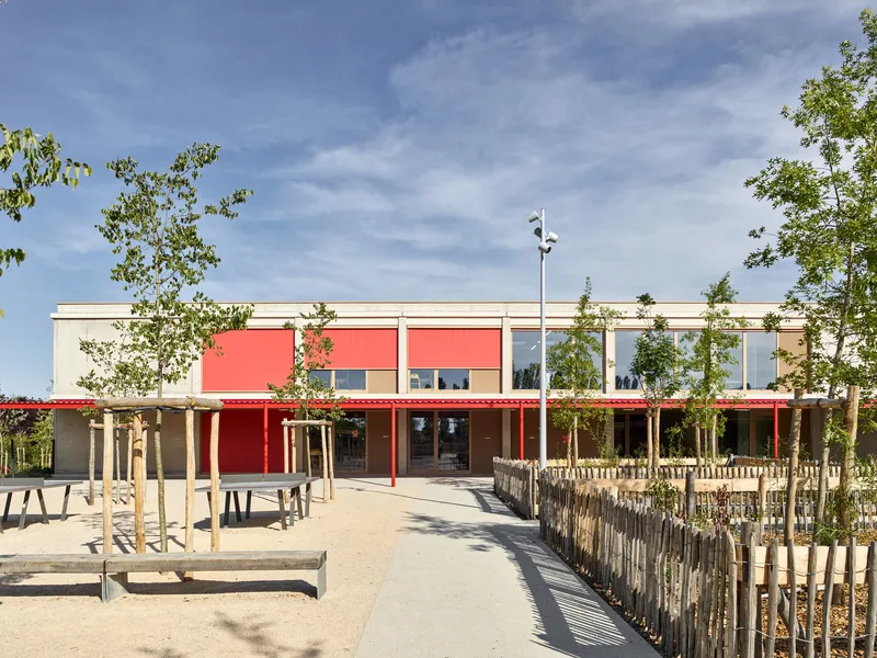 Entry sequence showing red canopy over timber columns and young planted trees in the forecourt