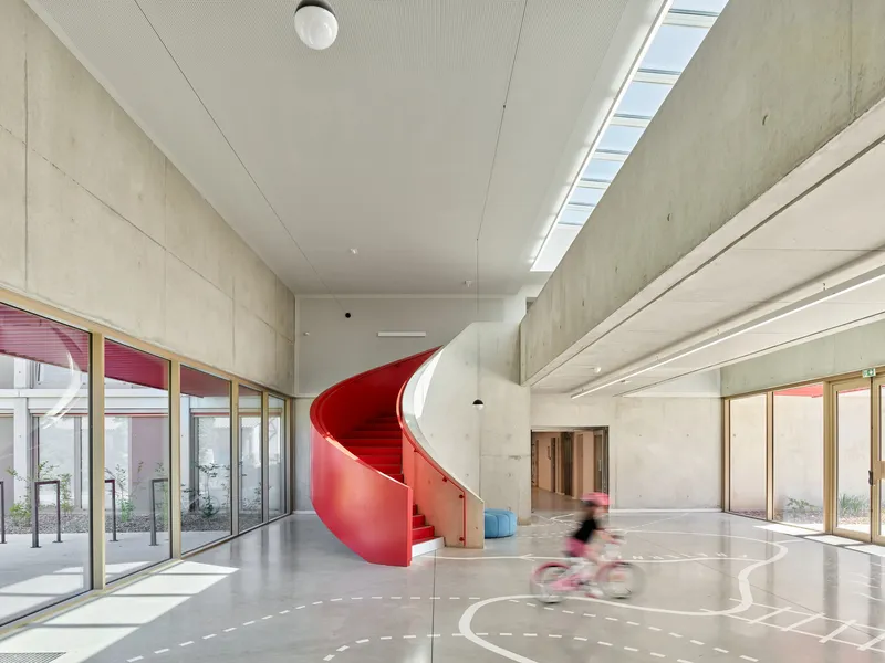 Red helical staircase connecting floors beside full-height glazing and concrete wall surfaces