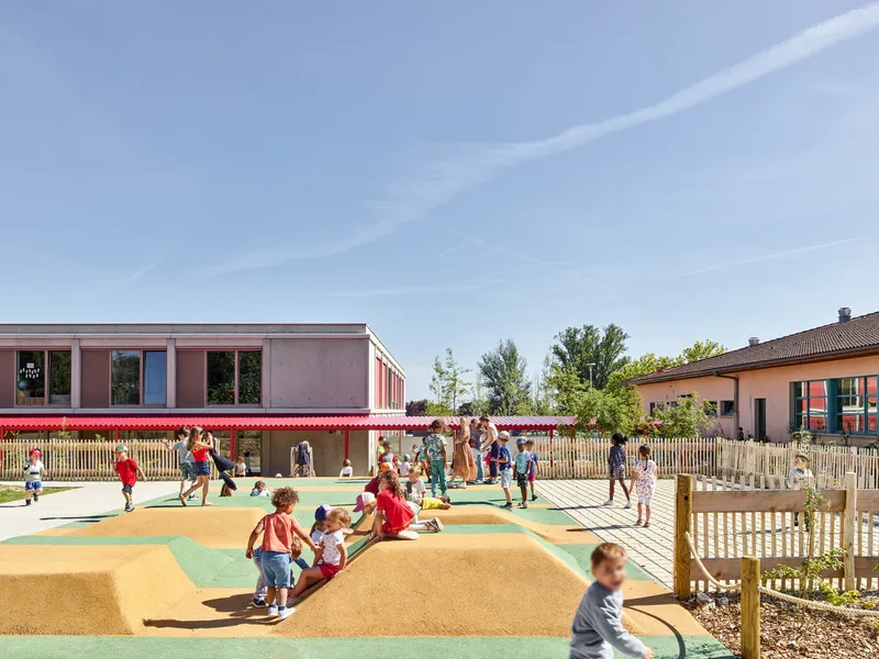 Playground with rubber surfacing and climbing mounds enclosed by timber picket fencing