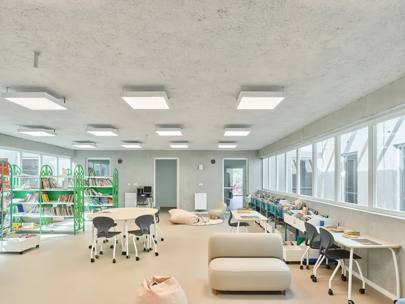 Classroom interior with square skylights puncturing the concrete ceiling and green book shelving along the wall
