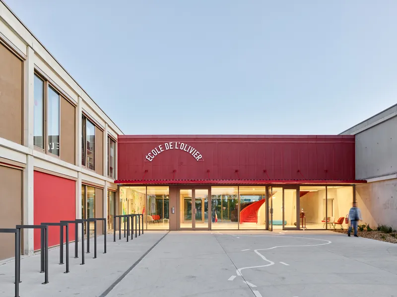 Glass entrance beneath red metal canopy with interior lighting at dusk