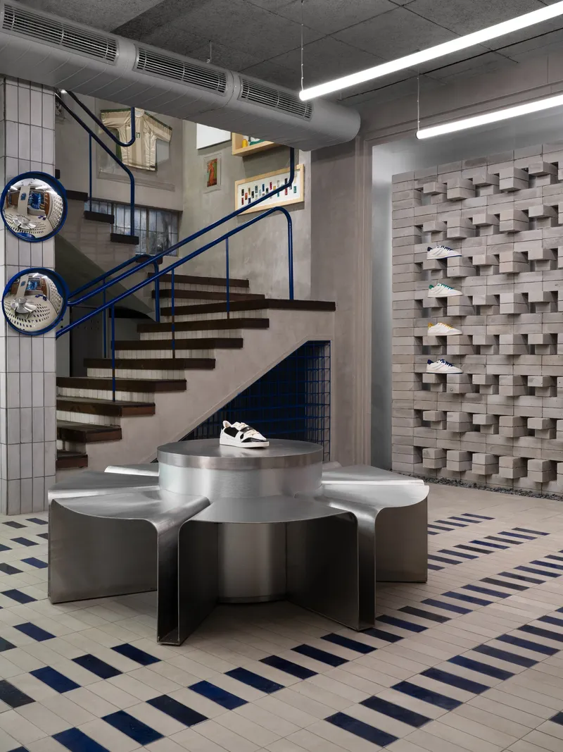 Floating timber stair with blue steel railing beside metal display pedestal and three-dimensional block wall