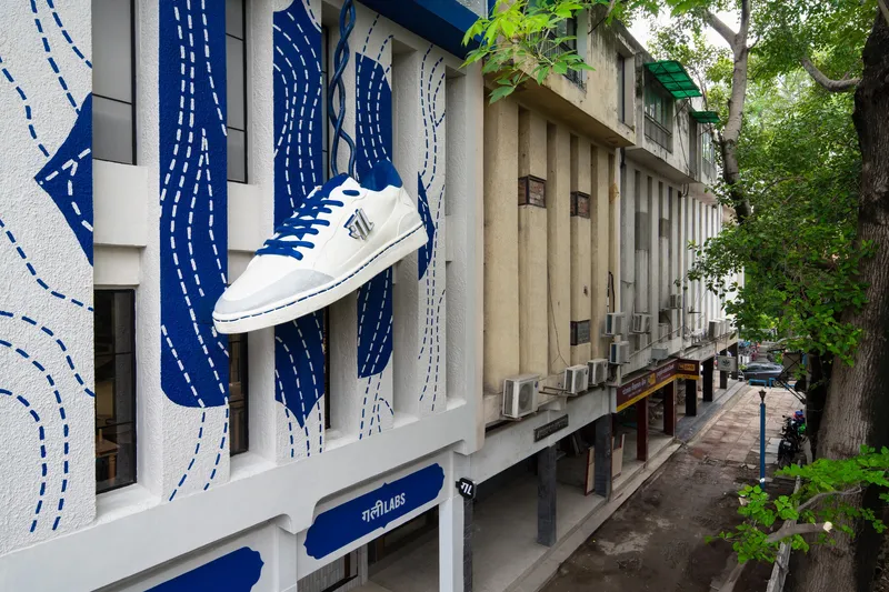 Angled street view showing the mural facade with oversized sneaker installation beneath overhanging tree branches