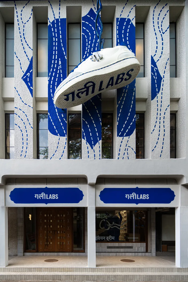 Close-up of the suspended white sneaker above the ground-level entrance with dual blue awnings