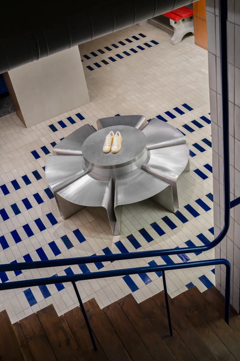 Looking down at stainless steel flower-shaped seating element on striped tile floor next to staircase