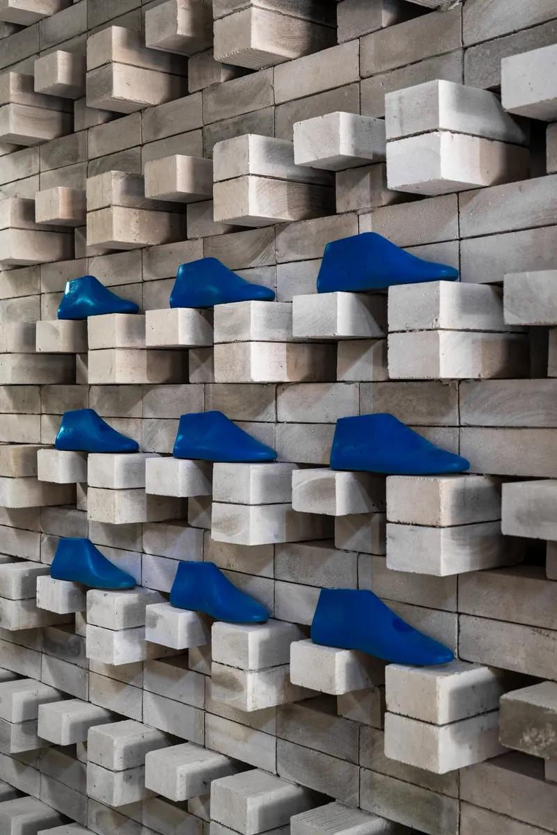 Close-up of staggered wood block wall with blue fabric footwear displayed on recessed ledges
