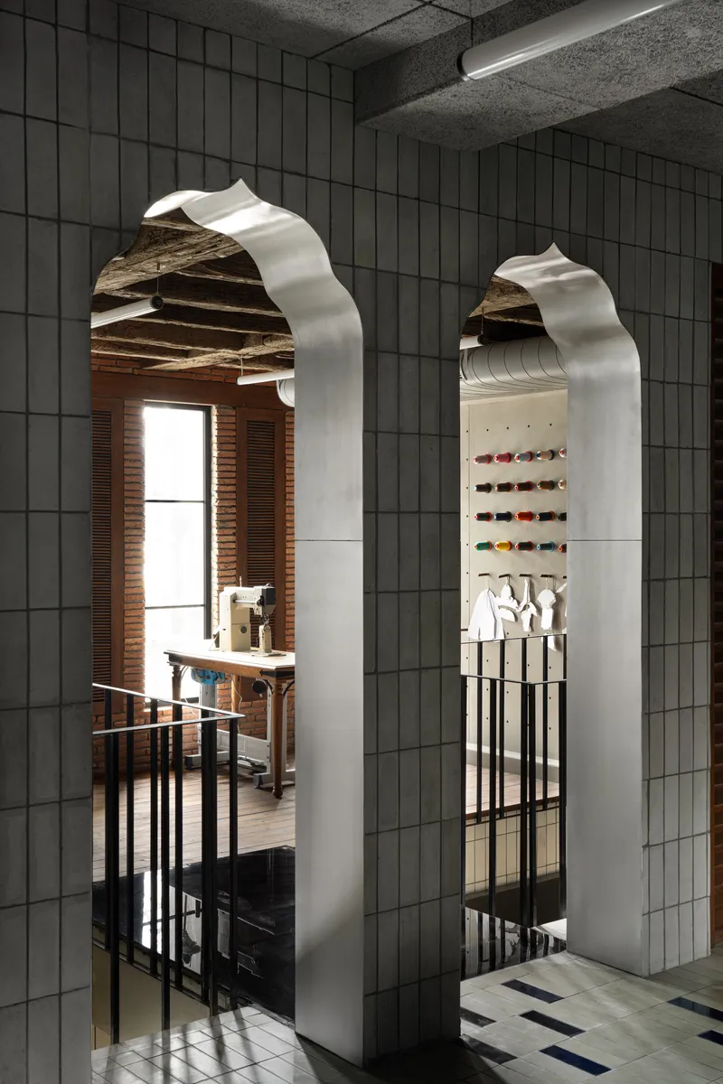 Two arched openings framed in white metal reveal a workspace with exposed timber beams and pegboard display