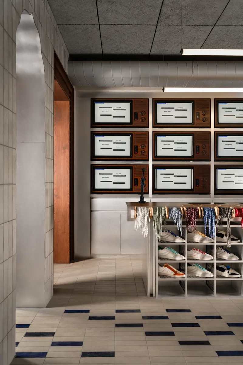 Corridor with grey tile walls leading to storage area displaying sneakers and backlit product boxes