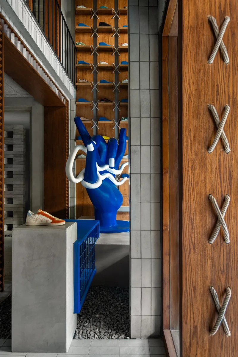Entryway detail with blue sculpture on concrete plinth beside timber wall with rope cross motifs and hexagonal shelving