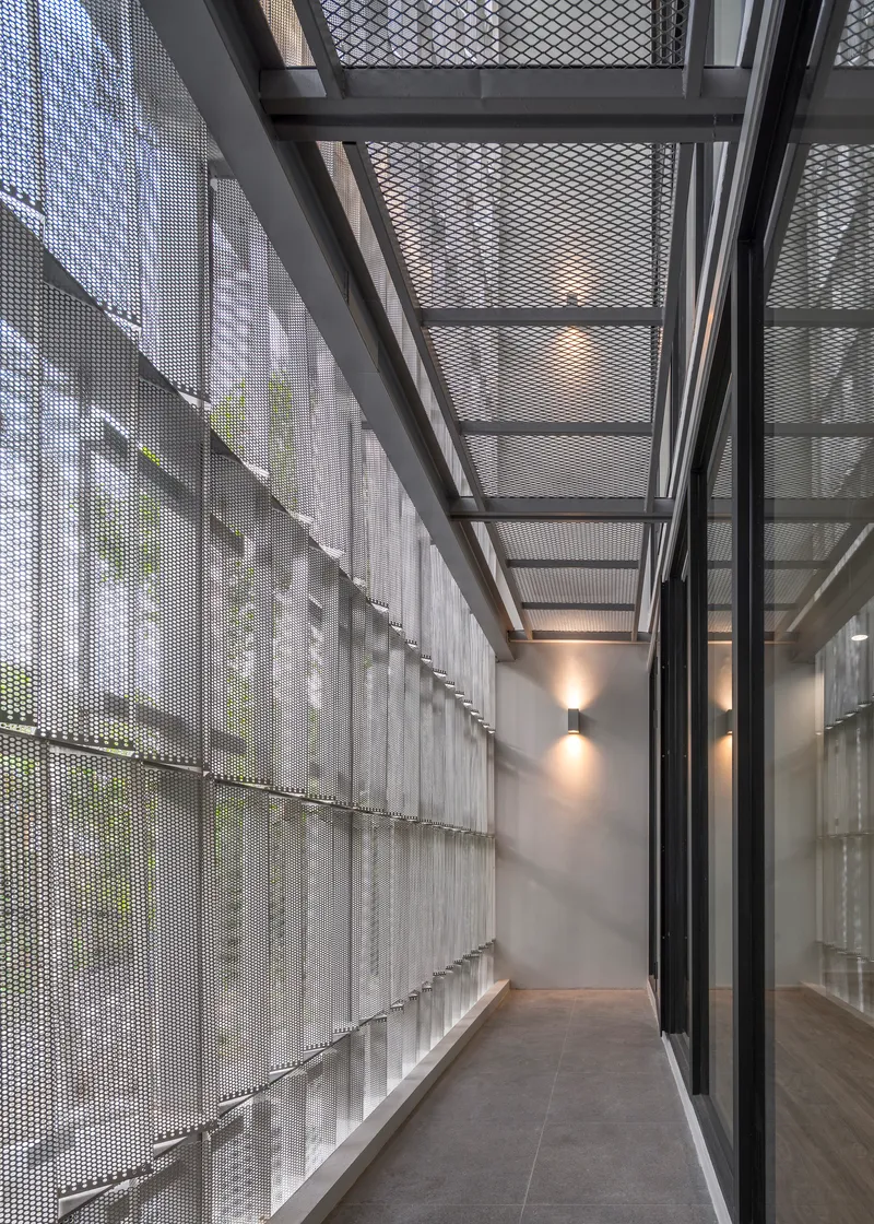 Narrow corridor with perforated metal screen wall and steel skylight structure overhead in diffused daylight