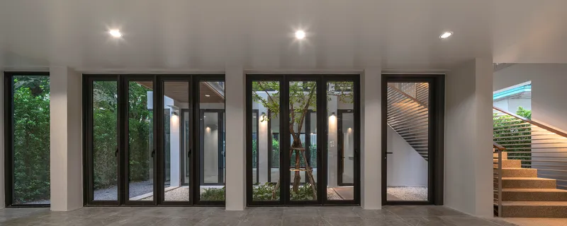 Interior room with black-framed glass doors opening to multiple planted courtyards at dusk