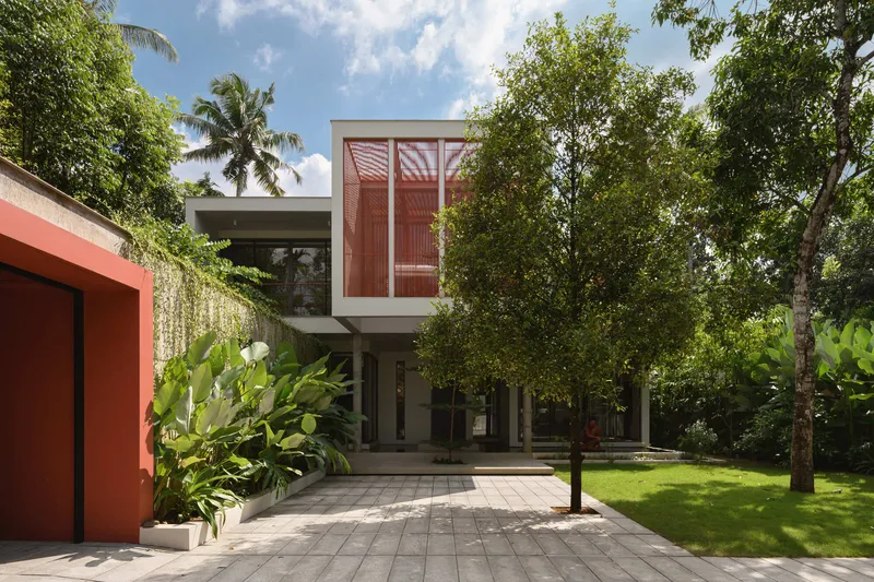 Elevated red screened volume on pilotis above garden courtyard with palm and deciduous trees
