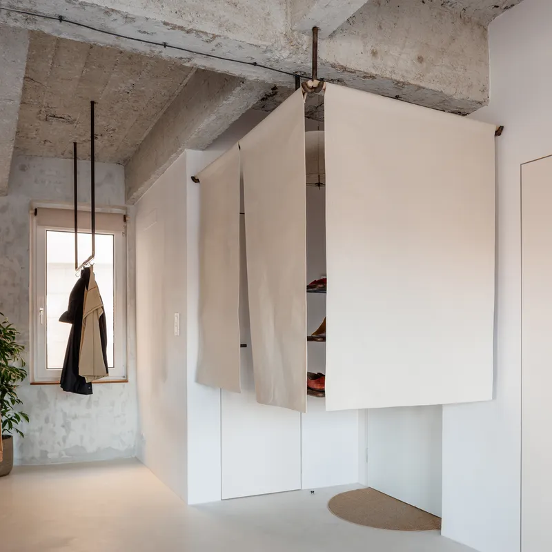 Corner storage unit with pivoting white panel revealing shelves beneath exposed concrete beams