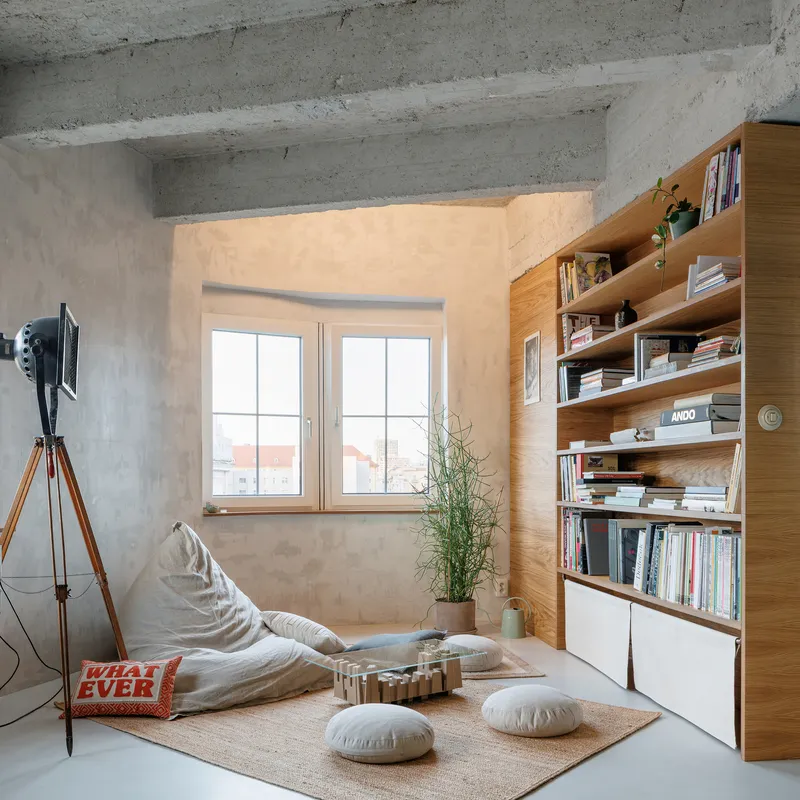 Oak shelving unit beside a double window with floor cushions and a potted plant below