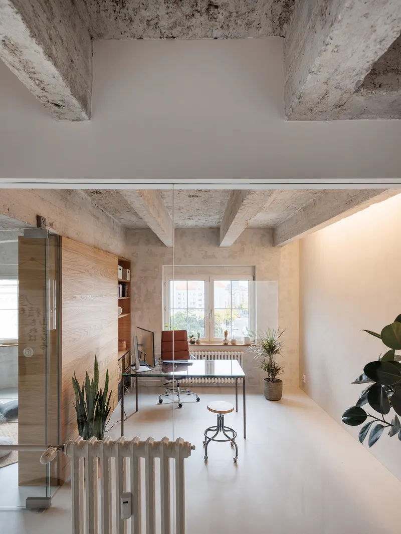 Long interior corridor with exposed concrete beams, white radiators, and desk area by the window