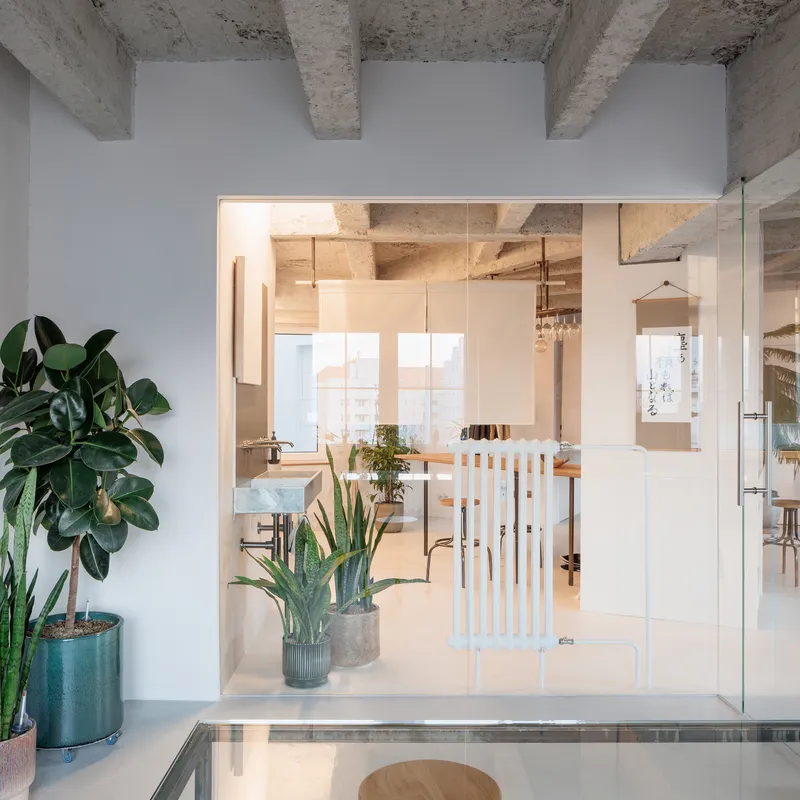 Glass partition with wooden slat divider separating rooms beneath exposed concrete vaulted ceiling
