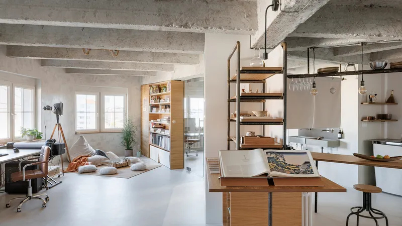Open plan interior with exposed concrete ceiling beams and timber shelving units beneath tall windows