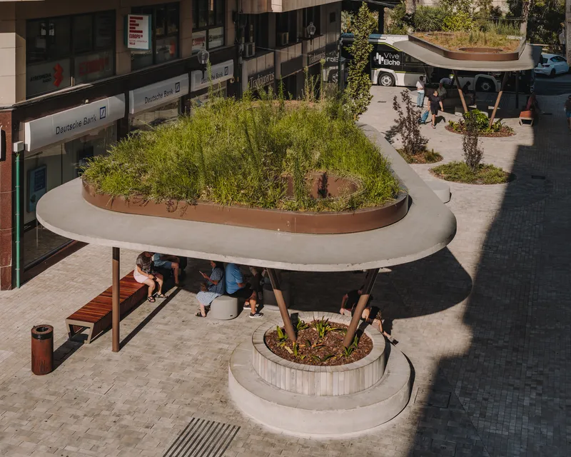 Elevated view of curved concrete canopies with planted roofs sheltering benches in a paved plaza