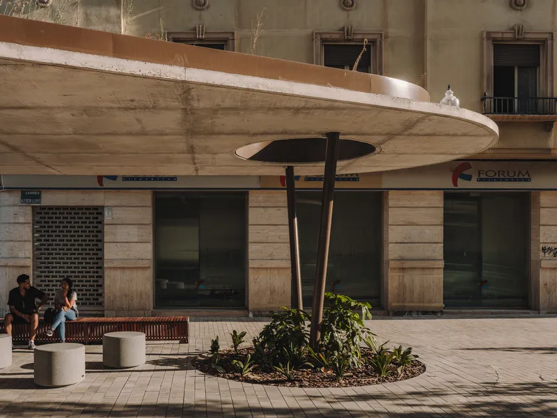 Concrete canopy with circular opening and central support column beside timber bench seating at dusk
