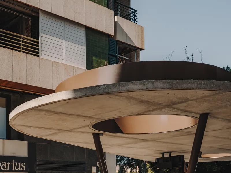 Underside detail of concrete canopy showing circular oculus and corten steel edging against overcast sky