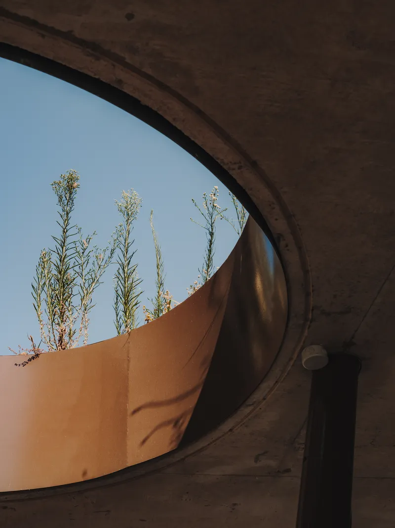 View through concrete arch framing corten steel planter with drought-tolerant grasses against clear sky