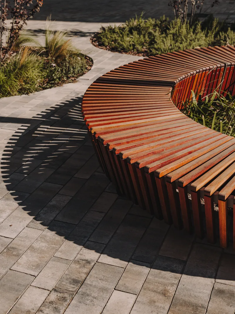 Curved slatted timber bench showing shadow pattern on dark paving tiles