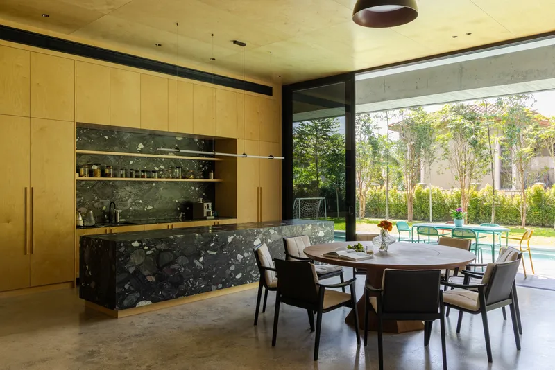 Kitchen and dining area with terrazzo island and plywood cabinetry opening to a garden courtyard