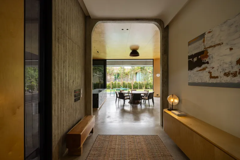 Entry corridor with board-formed concrete walls and an arched ceiling leading toward the dining space