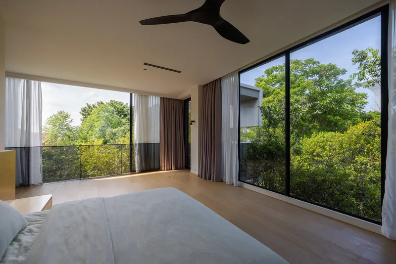Bedroom with floor-to-ceiling glazing and sheer curtains overlooking a canopy of green trees