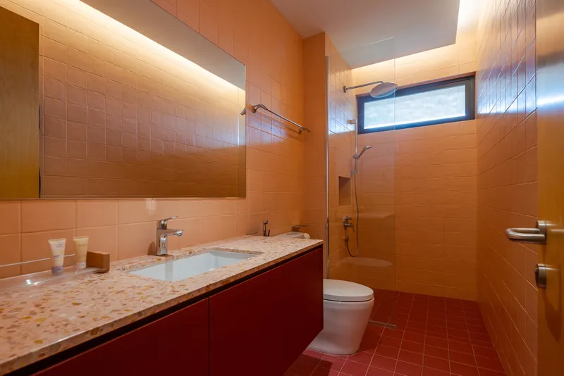 Bathroom with terrazzo counter, red cabinetry, and terracotta tile walls beneath a clerestory window