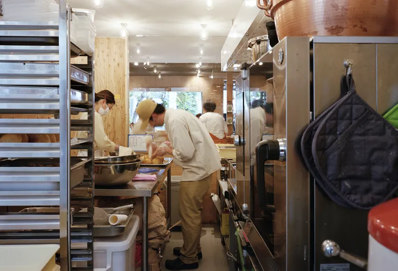 Staff working at stainless steel prep counter in narrow kitchen with track lighting overhead