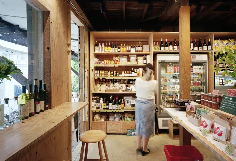 Plywood shelving and counter system with staff member reaching for products beneath exposed timber ceiling beams