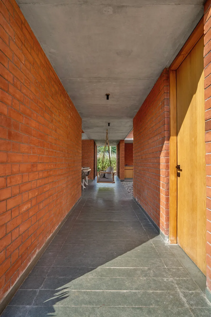 Covered corridor with red brick walls, concrete ceiling, and slate flooring leading to a planted courtyard