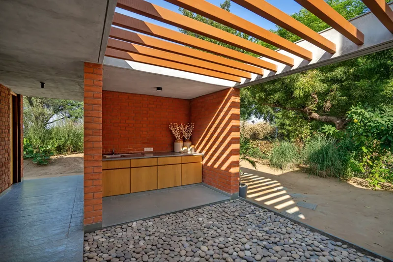 Courtyard with timber pergola overhead casting striped shadows across the pebble bed and concrete floor