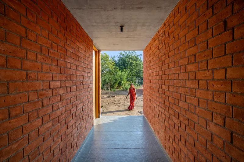 Corridor framed by exposed red brick walls leading to a figure in an orange sari