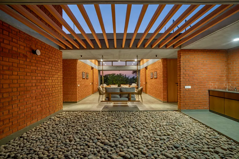 Interior courtyard with timber pergola, exposed rafters and pebbled floor at dusk