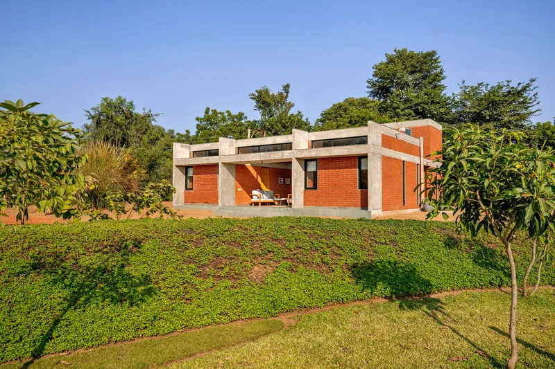Red brick facade with concrete frame set into a terraced lawn surrounded by fruit trees