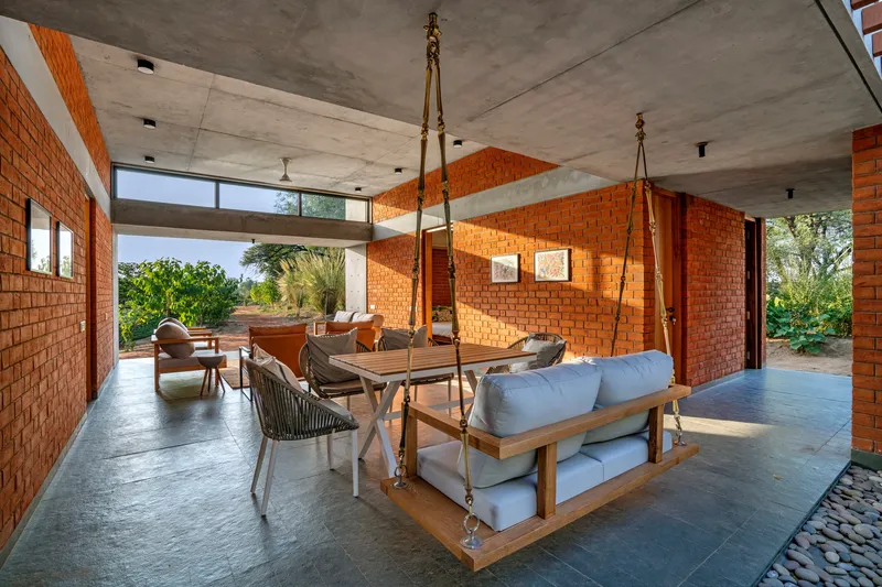 Open living area with exposed red brick walls, exposed concrete ceiling and suspended timber swing seat