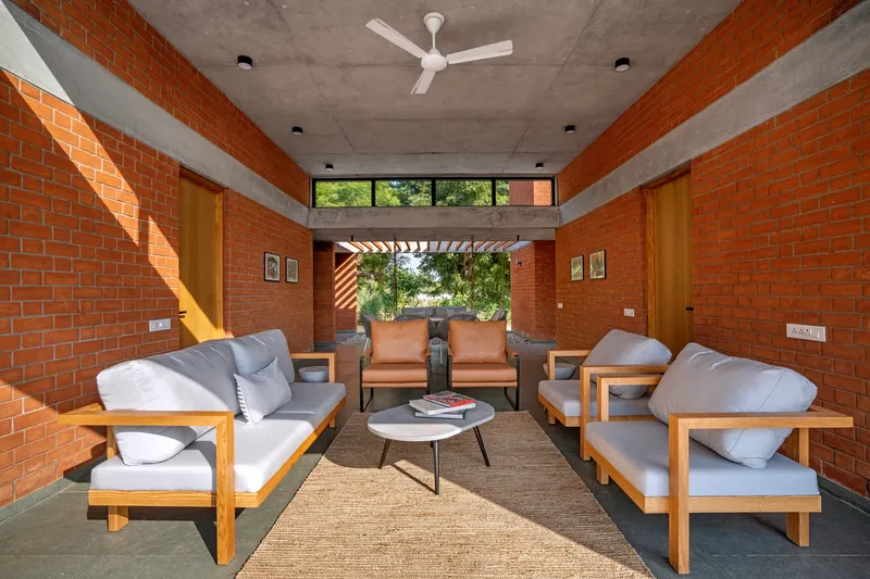Living room with red brick walls framing a view through a slatted pergola to the landscape beyond