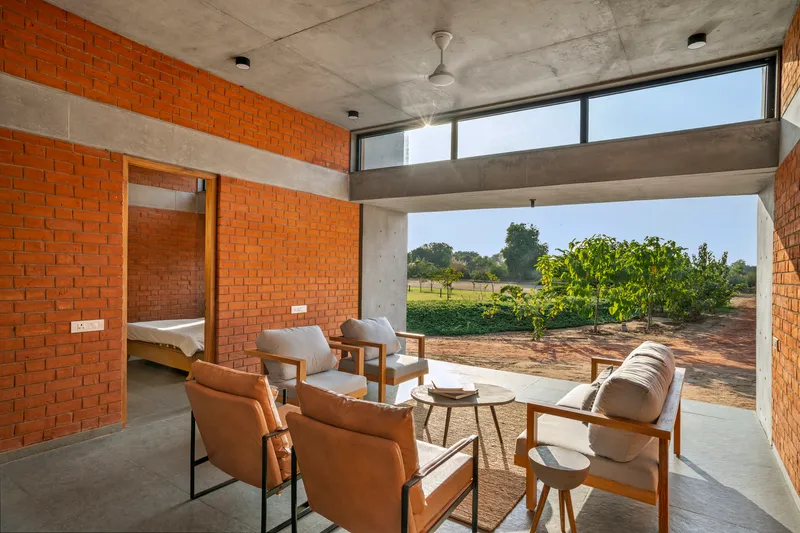 Interior seating area opening to agricultural fields through a wide concrete-framed aperture in morning light