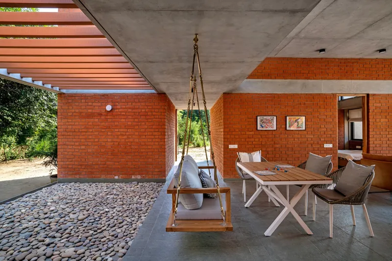Covered terrace with pebble floor, suspended swing and louvered ceiling filtering afternoon sunlight
