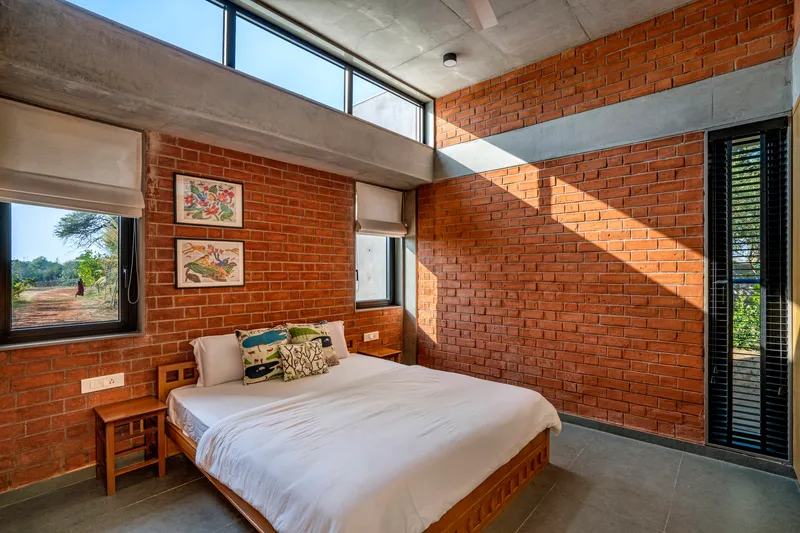 Bedroom with red brick walls, concrete ceiling beam, and clerestory windows casting geometric shadows