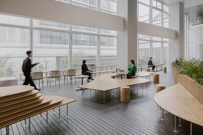 Open seating area with kidney-shaped plywood tables and wire-backed chairs facing clerestory windows in muted daylight