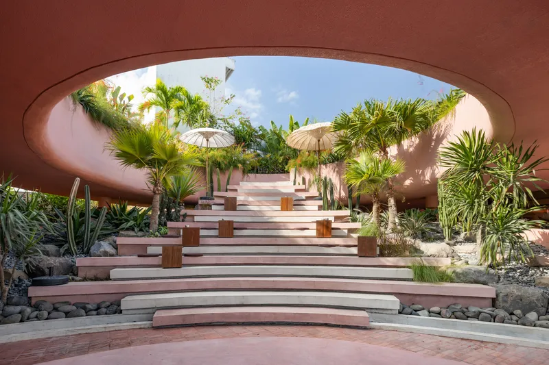 Wide steps leading through an elliptical opening framing palms and white parasols above