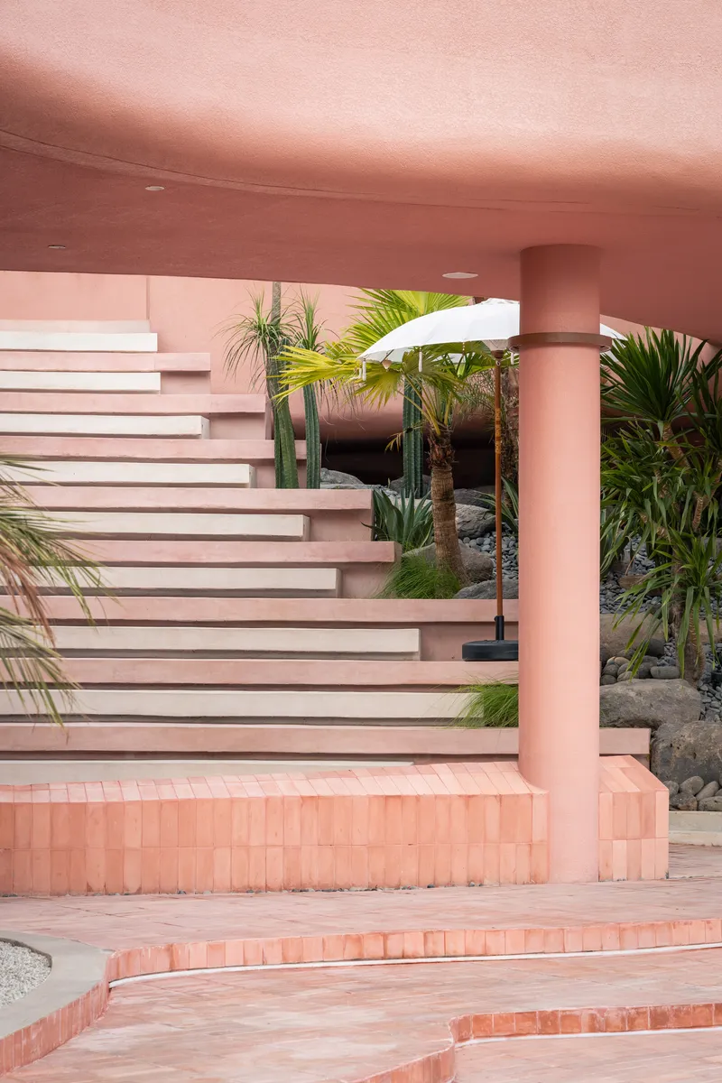 Cantilevered stair treads in pink and white beneath a continuous curved soffit with potted palms and umbrella
