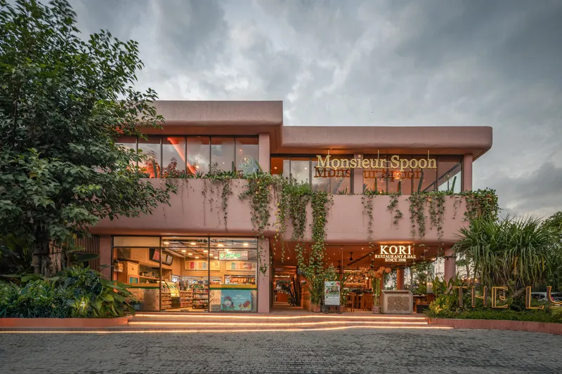 Two-story retail facade with flat overhanging roof and illuminated storefronts at dusk under heavy clouds