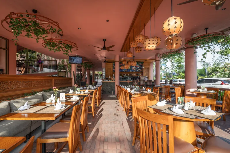 Open-air restaurant dining area with timber tables and pendant lighting surrounded by cylindrical columns and tropical plants