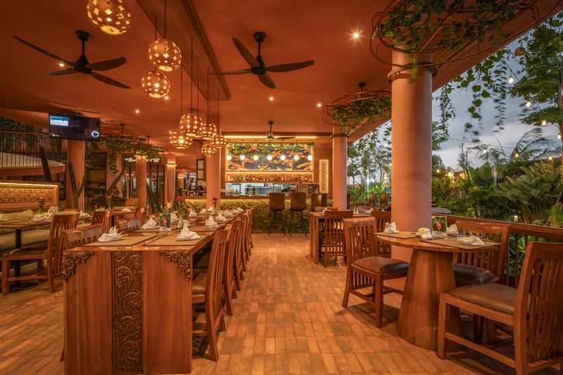 Restaurant interior with carved timber tables and spherical pendant lights under a terracotta ceiling at twilight