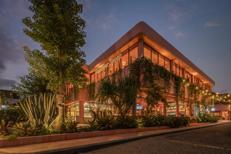Two-story facade with continuous glazing and planted terrace illuminated at dusk